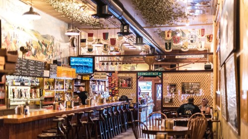 A cozy bar interior with wooden furniture, colorful murals, and a variety of beer taps, creating a warm atmosphere.