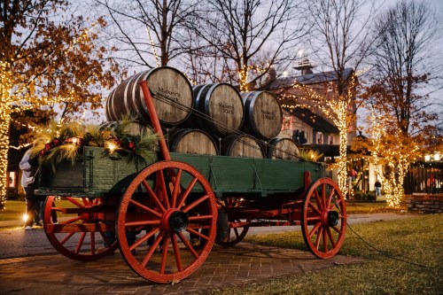 A festive wagon with barrels, decorated with greenery, surrounded by twinkling lights in a cozy outdoor setting.