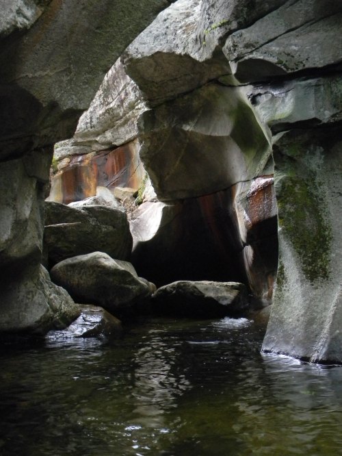 A serene rock formation with water flowing through, creating a natural archway and reflecting light.