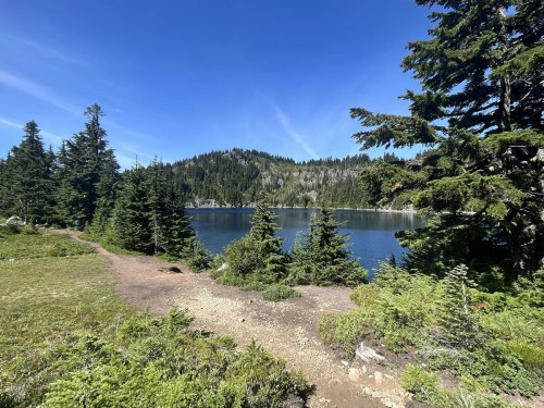 A serene lake surrounded by lush green trees and mountains under a clear blue sky.