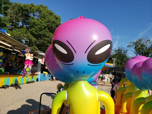 Colorful alien inflatable with large eyes, set against a bright blue sky at a fair or carnival.