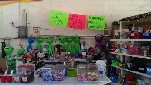 A colorful display of alien balloons, snacks, and raffle items at a market stall with bright signs.