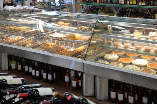 A display case filled with various baked goods and desserts, with bottles of wine visible in the foreground.
