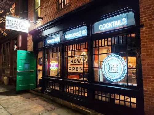 A restaurant with a green door, featuring signs for burgers, cocktails, and craft beer, illuminated at night.