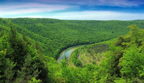 Lush green hills surround a winding river under a blue sky, showcasing a serene natural landscape.