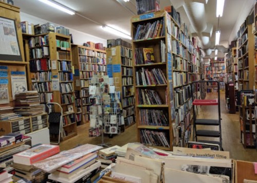 A cozy bookstore filled with tall shelves of books, wooden floors, and a few tables scattered throughout.