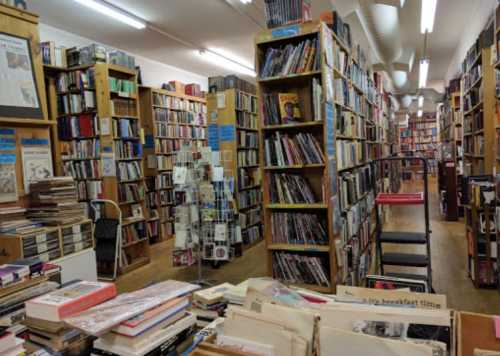 A cozy bookstore filled with tall shelves of books, wooden floors, and a few tables scattered throughout.