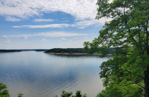 A serene lake surrounded by lush greenery under a partly cloudy sky.