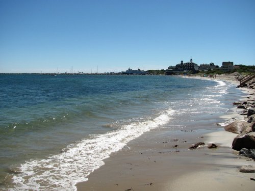 A serene beach scene with gentle waves lapping at the shore and a distant view of buildings along the coastline.