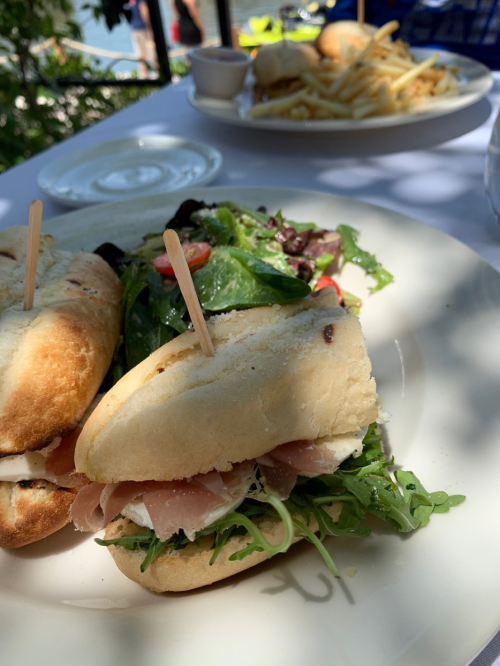 A close-up of a sandwich with greens and a side salad, with another plate of fries and burgers in the background.