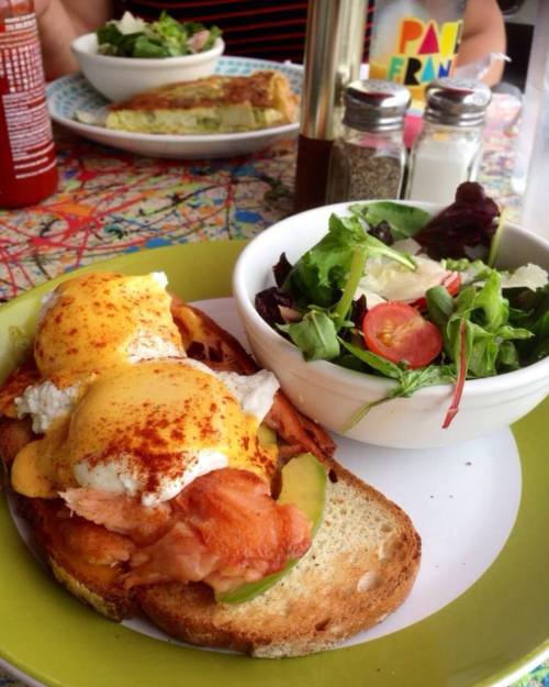 A plate with eggs Benedict on toast, topped with salmon and paprika, alongside a small salad in a bowl.