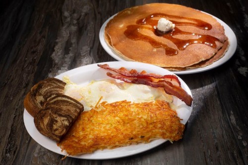 A plate of breakfast featuring eggs, hash browns, bacon, toast, and a side of pancakes with syrup and butter.