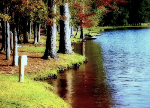 A serene lakeside scene with colorful autumn trees reflecting in the water, and a small boat visible in the distance.