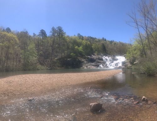 A serene landscape featuring a waterfall cascading into a calm river, surrounded by lush greenery and blue skies.