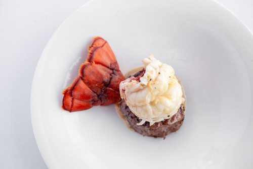 A plate featuring a tender beef filet topped with a lobster tail, drizzled with a light sauce.