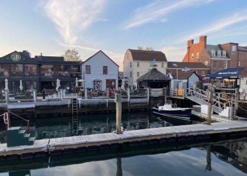 A scenic harbor view with boats, docks, and charming buildings along the waterfront under a clear sky.