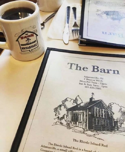 A coffee cup beside a menu featuring "The Barn" restaurant in Adamsville, RI, with a sketch of the building.