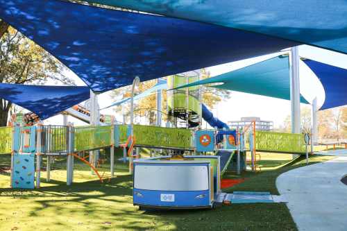 Colorful playground with climbing structures and shaded areas, surrounded by green grass and trees.