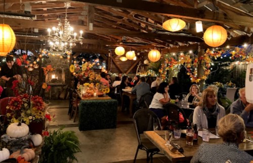 Cozy indoor dining area decorated with autumn flowers, lanterns, and a chandelier, with guests enjoying their meals.