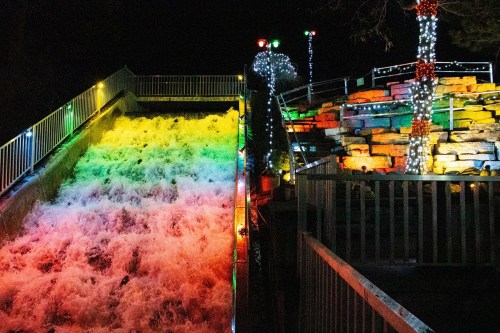 A brightly lit water slide at night, with colorful lights illuminating the cascading water and surrounding rocks.