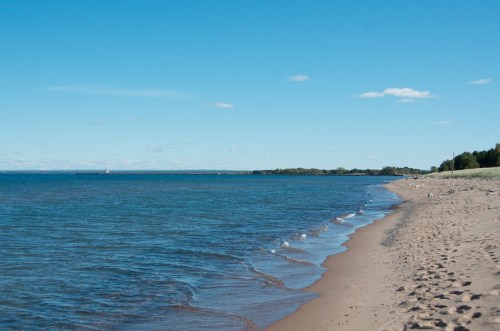 A serene beach scene with gentle waves lapping at the sandy shore under a clear blue sky.
