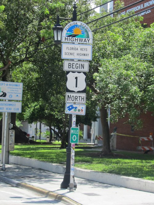 Signpost indicating the start of Florida Scenic Highway, with markers for Mile 0 and Highway 1 North. Lush greenery in background.