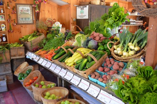 A vibrant display of fresh vegetables and fruits in a rustic market, featuring baskets of greens, potatoes, and apples.