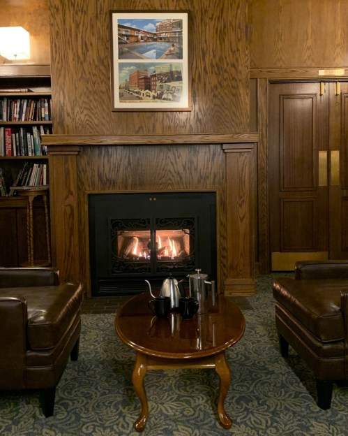 Cozy sitting area with a fireplace, two leather chairs, a wooden table, and a framed artwork on the wall.