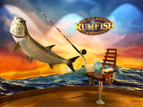 A fishing chair with a rod against a colorful mural of a large fish and ocean waves at RumFish Grill.