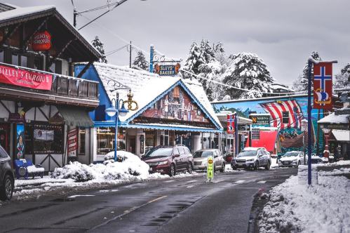 Snow-covered street lined with colorful shops and festive decorations in a quaint village.