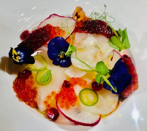 A vibrant dish featuring scallops, colorful garnishes, edible flowers, and caviar on a white plate.