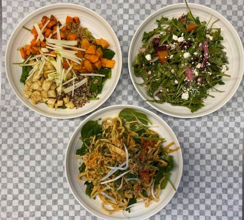 Three bowls of colorful salads: one with quinoa and sweet potatoes, one with mixed greens and feta, and one with noodles and veggies.