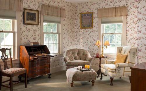 Cozy room with floral wallpaper, a vintage writing desk, armchairs, and soft lighting from table lamps.
