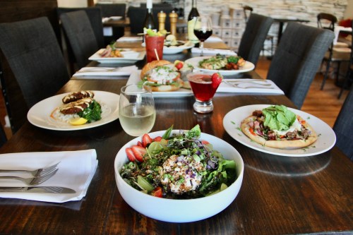 A table set with various dishes, including salads, drinks, and entrees, in a cozy restaurant setting.