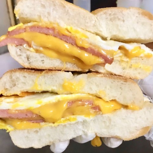 A close-up of a sandwich with layers of ham, melted cheese, and egg between two slices of soft white bread.