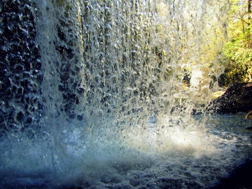A close-up view of cascading water from a waterfall, creating a misty spray against a serene natural backdrop.