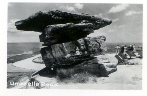 Black and white photo of Umbrella Rock, a large rock formation with a flat top, overlooking a scenic landscape.