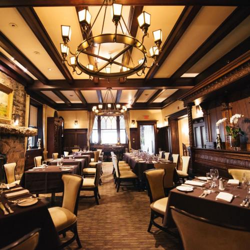 Elegant restaurant interior with wooden accents, chandeliers, and neatly set tables ready for dining.
