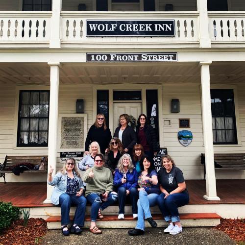 A group of women poses together on the porch of Wolf Creek Inn, smiling and enjoying their time.