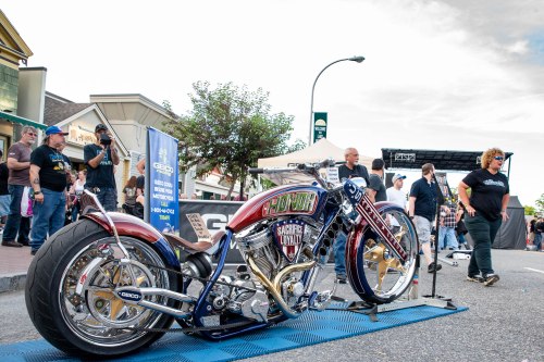 A custom motorcycle with a vibrant red and blue design, displayed at an outdoor event with people in the background.