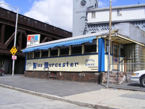 A vintage diner named "Miss Worcester" with a blue awning, located near a railway bridge.