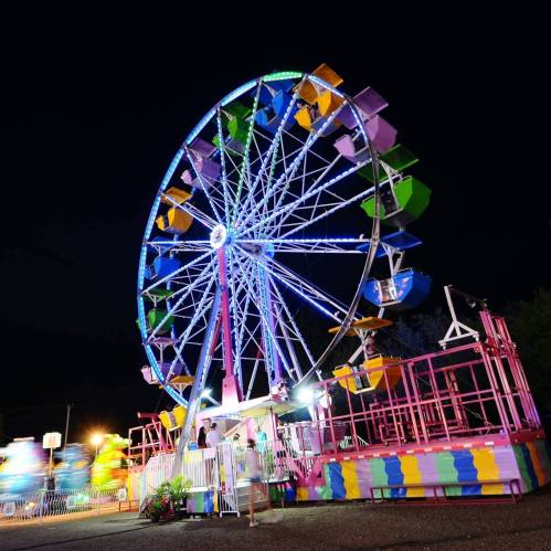 A brightly lit Ferris wheel at night, surrounded by colorful lights and a festive atmosphere.