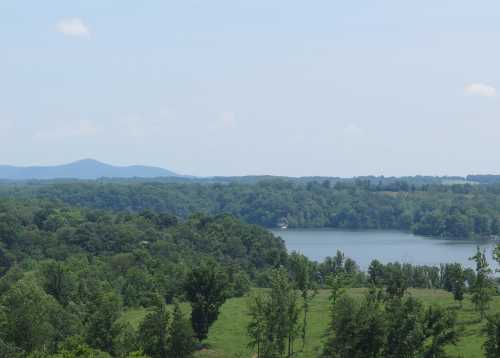 A serene landscape featuring a lake surrounded by lush greenery and distant mountains under a clear blue sky.