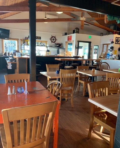 Interior of a casual restaurant with wooden tables and chairs, a bar area, and a warm, inviting atmosphere.