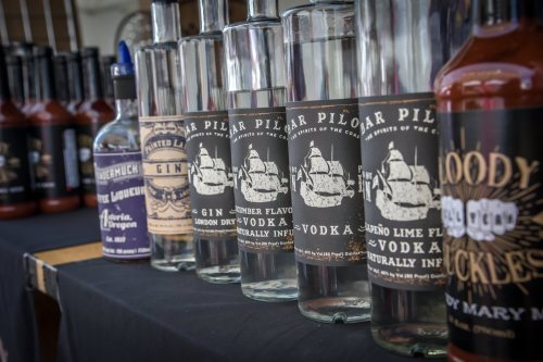 A display of various bottles of spirits, including gin and flavored vodka, on a table at a market or event.