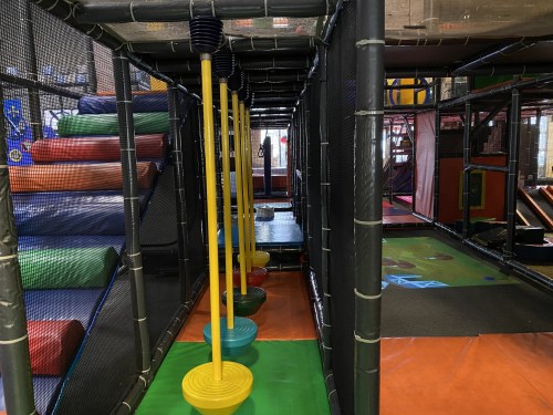 A colorful indoor play area featuring climbing structures, slides, and hanging rings for children.
