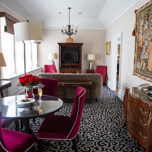 A cozy living room with a chandelier, a TV, a dining table, and plush chairs, featuring elegant decor and a patterned carpet.