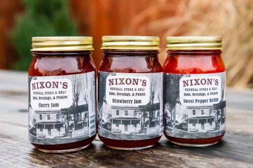 Three jars of Nixon's jams and relishes: Cherry Jam, Strawberry Jam, and Sweet Pepper Relish, displayed on a wooden table.