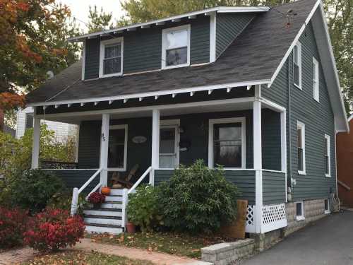 A charming green house with a front porch, surrounded by colorful foliage and a well-maintained garden.