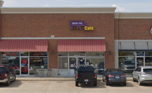 Exterior of Neon Pig Cafe, a brick building with red awnings, featuring parked cars and a clear blue sky.